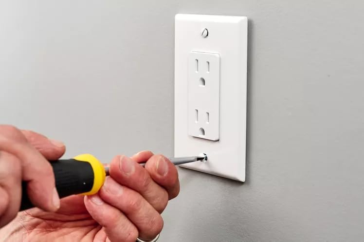 A person securing the faceplate onto the installed AES Spy Cameras wall outlet camera with a screwdriver.