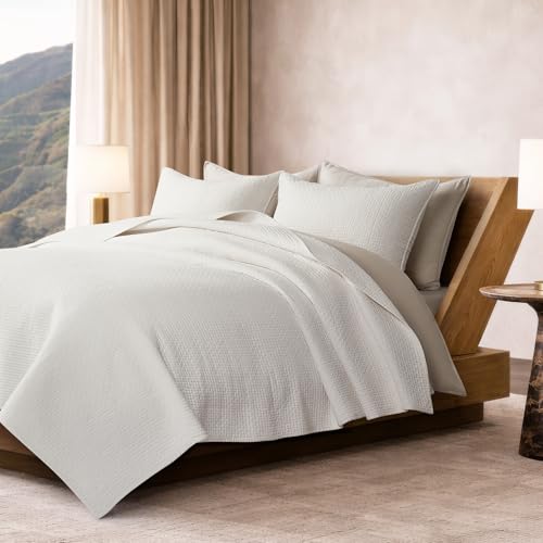 Bright bedroom with white quilted bedding and pillows arranged on a wooden platform bed