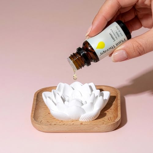 A hand adding a drop of lemon essential oil to a white ceramic flower diffuser.