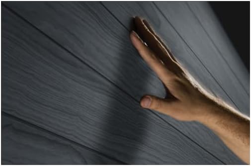 Close-up of the wood-like texture of the Keter Woodium 757-5 resin shed wall, with a hand touching it.