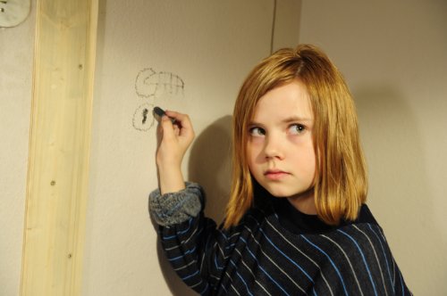 Still from 3096 Days showing a young girl drawing on a wall with chalk.