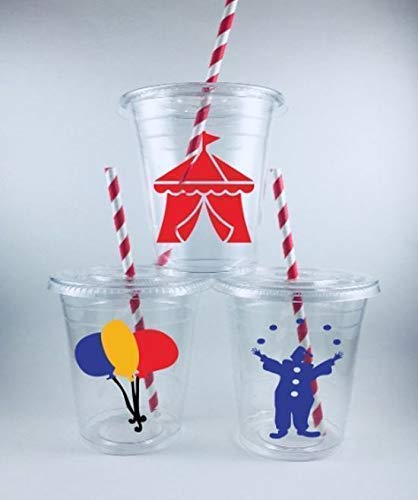 Three clear plastic party cups with red and white striped straws. One cup has a red circus tent decal, another has blue, yellow, and red balloon decals, and the third has a blue clown juggling decals.