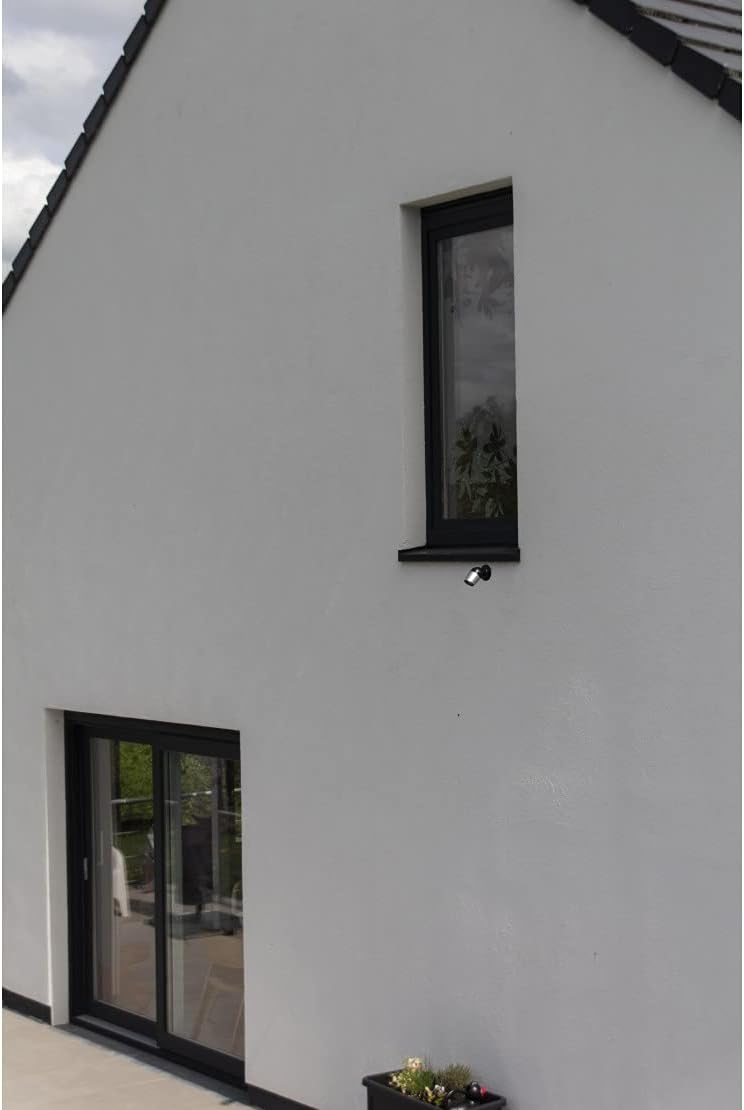 Chacon IP Wi-Fi HD Outdoor Camera mounted on the exterior wall of a modern house, positioned below a window.