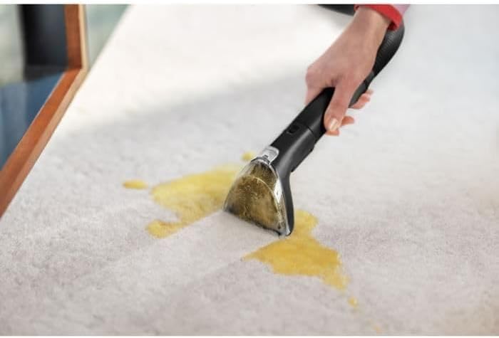 Person cleaning a yellow spill on a white carpet with the BISSELL SpotClean Mini
