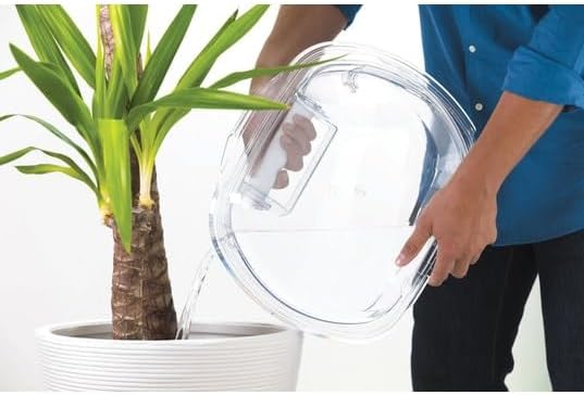 A person emptying the clear water collection tank from the dryer door into a plant pot.
