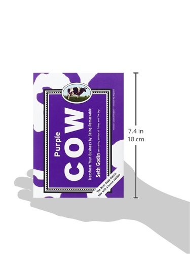 A hand holding the Purple Cow book, with measurements indicating its dimensions: 7.4 inches or 18 cm in height.