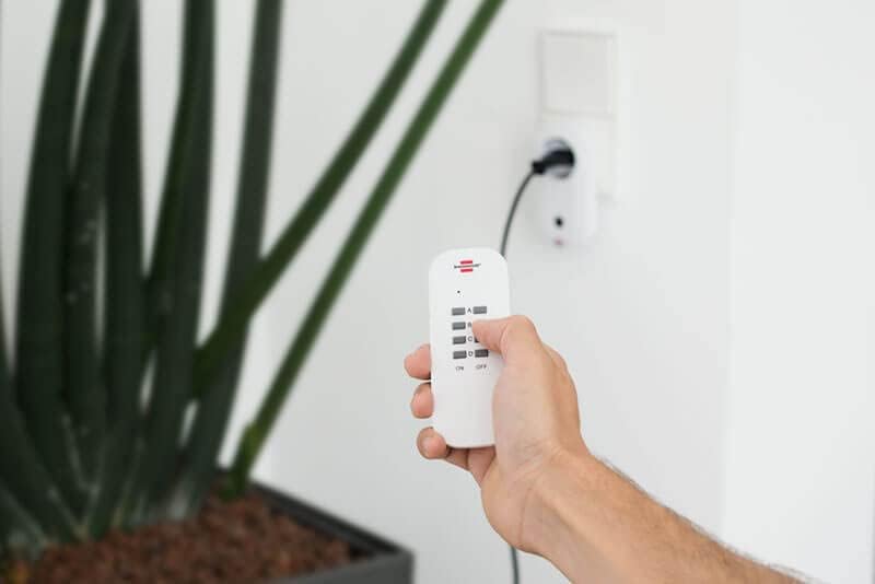 A hand holding the Brennenstuhl 4-channel remote control, ready to operate the wireless sockets.