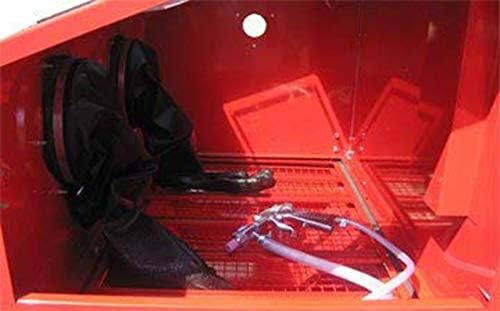 Interior view of the sandblaster cabinet showing the integrated rubber gloves and the blasting gun with its hose.