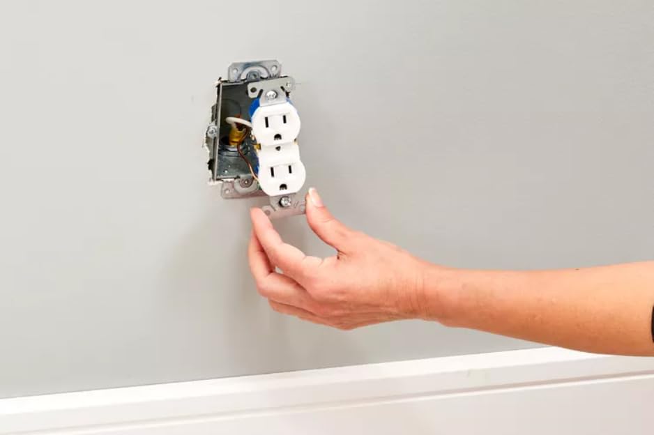 A hand gently pushing the wired outlet camera into the wall box.