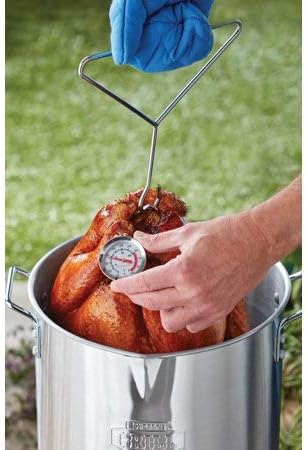 A hand inserting a meat thermometer into the thigh of a fried turkey, which is still in the pot.