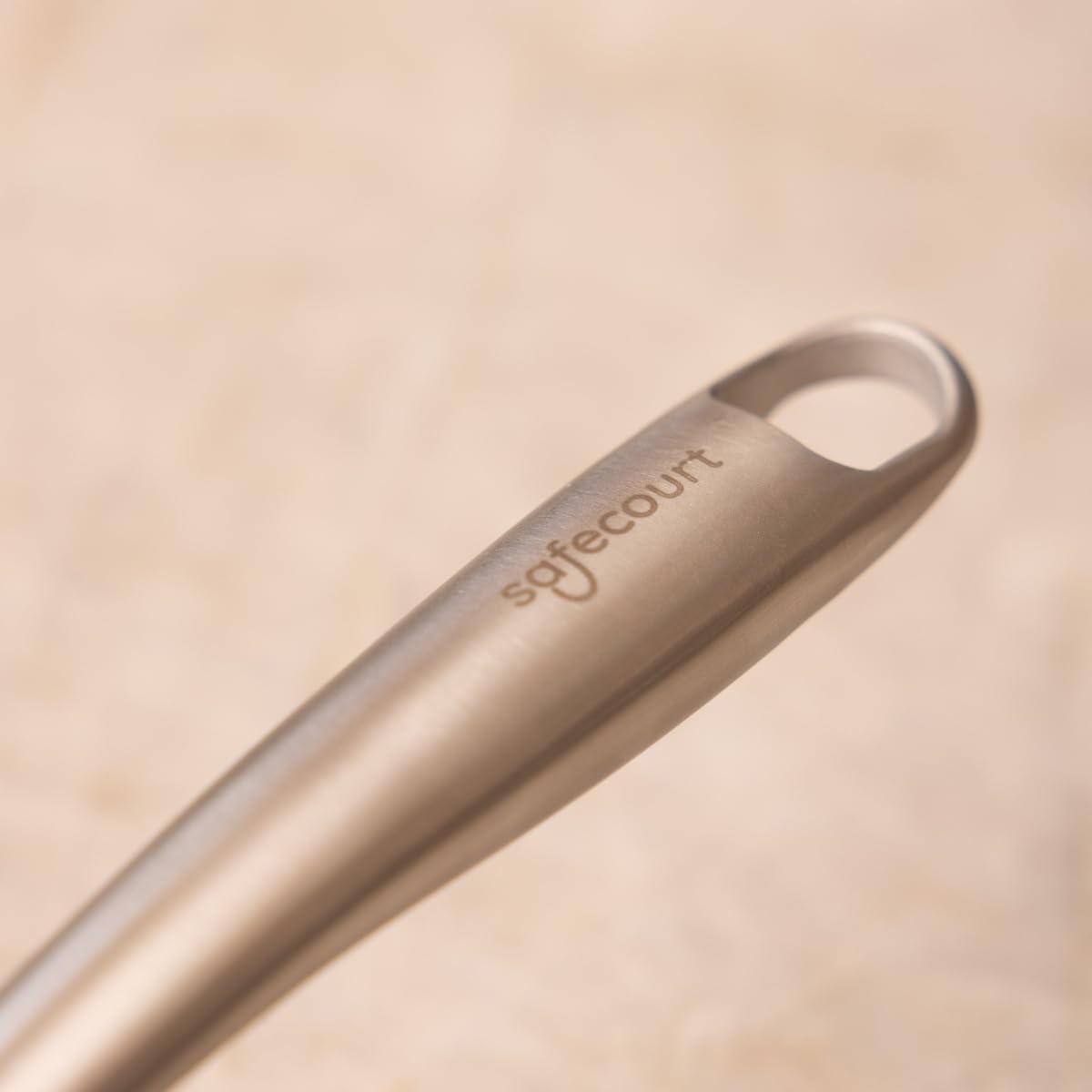 Close-up of the brushed stainless steel handle of the Safecourt frying pan with 'safecourt' engraved.