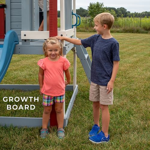 Image of Backyard Discovery Beacon Heights Elevated Cedar Wooden Kids Playhouse with Wave Slide, Play Kitchen, Wrap-Around Deck, Flat-Step Ladder, Half Door, Windows, Bell, and Growth Chart for Outdoor Play