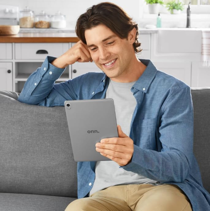 A person sitting on a couch, holding and looking at the onn. 10.1 inch tablet, demonstrating typical usage.