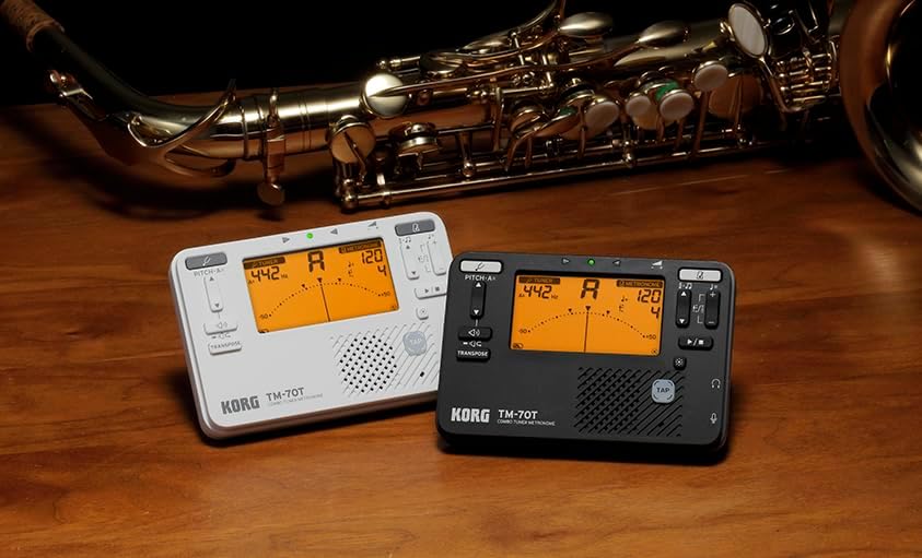 Two Korg TM-70T units, black and white, next to a flute and saxophone