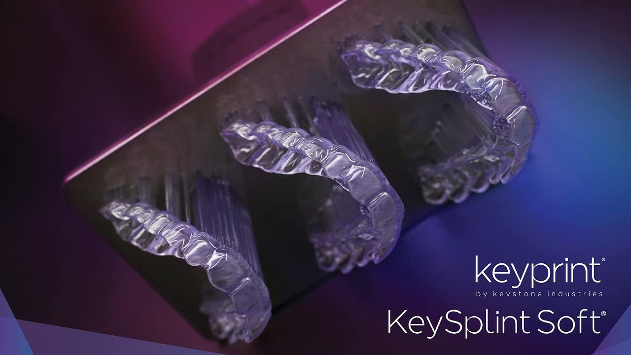Multiple clear dental splints being 3D printed on a build plate, still attached to supports.
