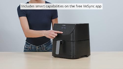 Person pressing the touch display on a black COSORI Pro Gen 2 air fryer on a countertop, with its pull-out basket and handle visible