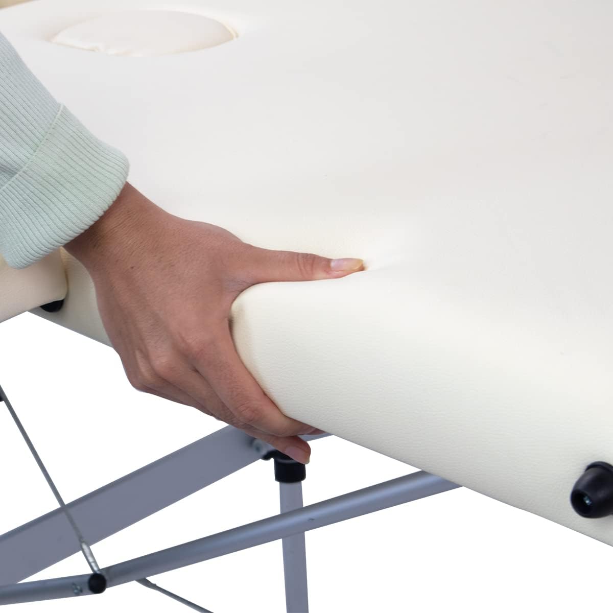 Close-up of a hand pressing on the Mobiclinic massage table's cream-colored faux leather cushion