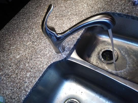 Kitchen faucet in use, water running into a double sink