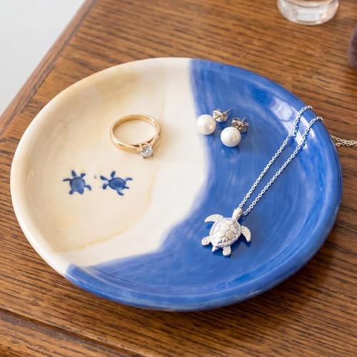 a small blue ceramic ring dish with a sea turtle design in the center, holding a ring
