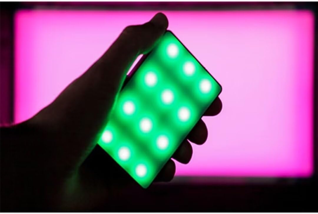 A hand holding the Aputure Amaran MC light, emitting a green color.