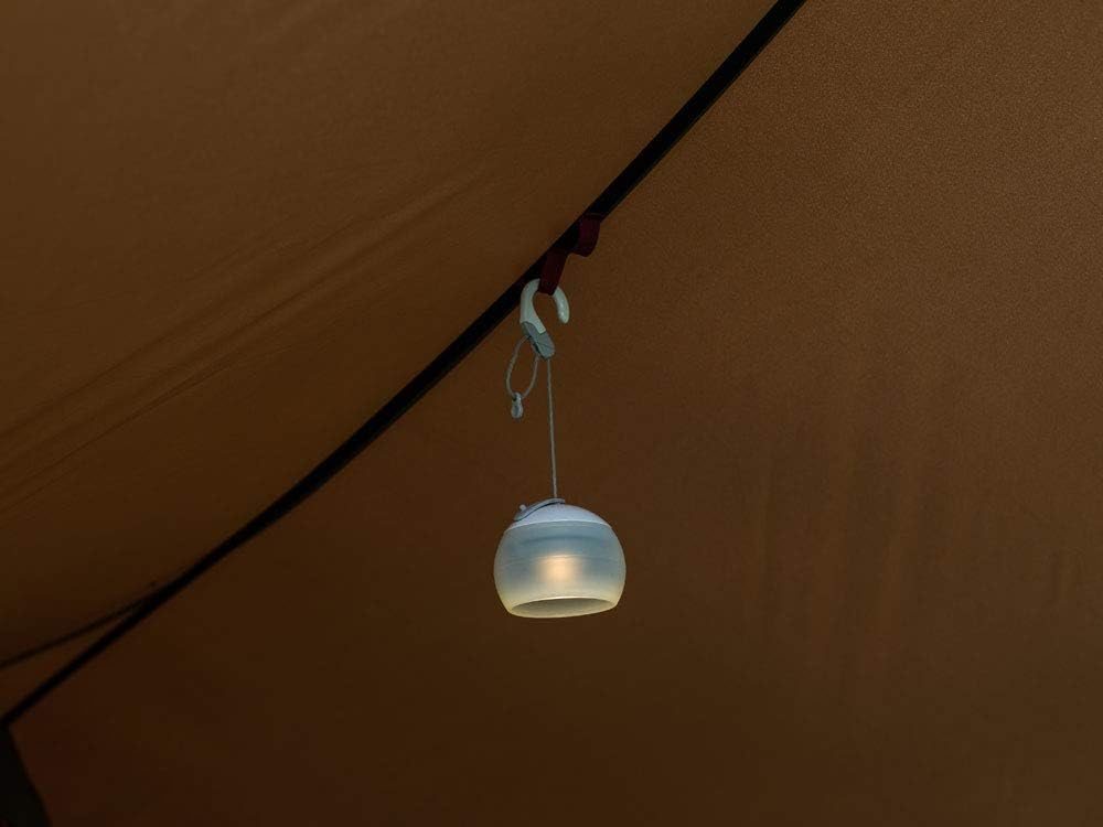 A small camping lantern hanging from a loop inside the Snow Peak Tarp, providing illumination.