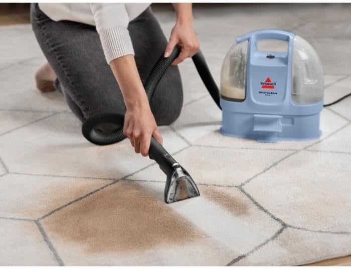 Person cleaning a large stain on a patterned carpet with the BISSELL SpotClean Mini