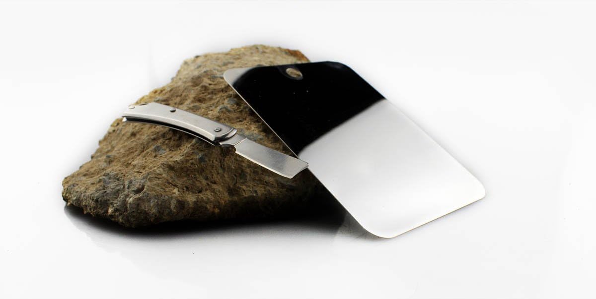 SE Double-Sided Outdoor Mirror next to a small folding knife on a rock