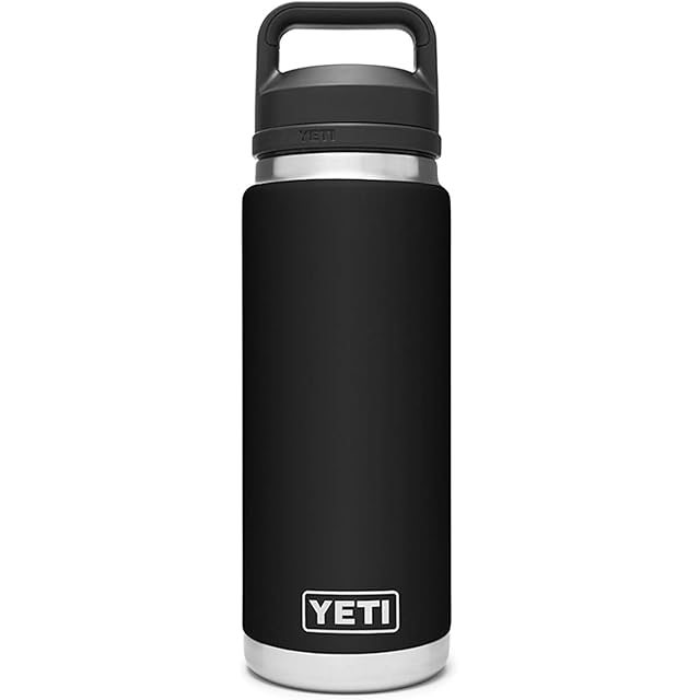YETI Rambler 26 oz Bottle Vacuum Insulated Stainless Steel with Chug Cap in classic black DuraCoat finish on a wooden gym bench, the screw-on Chug Cap with TripleHaul handle visible, the no-straw outdoor and jobsite pick for buyers who want forklift-survivable build