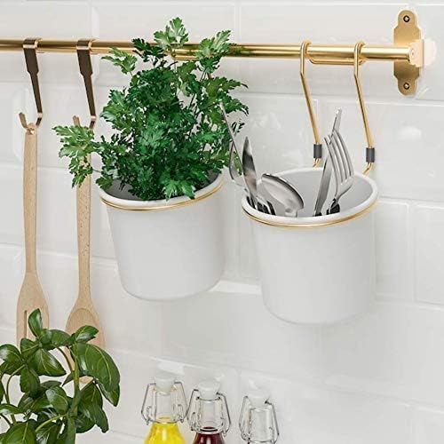 IKEA Hultarp Rail in polished brass color, mounted on a white tiled wall, holding two white containers. One container holds a green plant, and the other holds kitchen utensils like forks and spoons. Wooden spatulas hang from hooks on the rail.