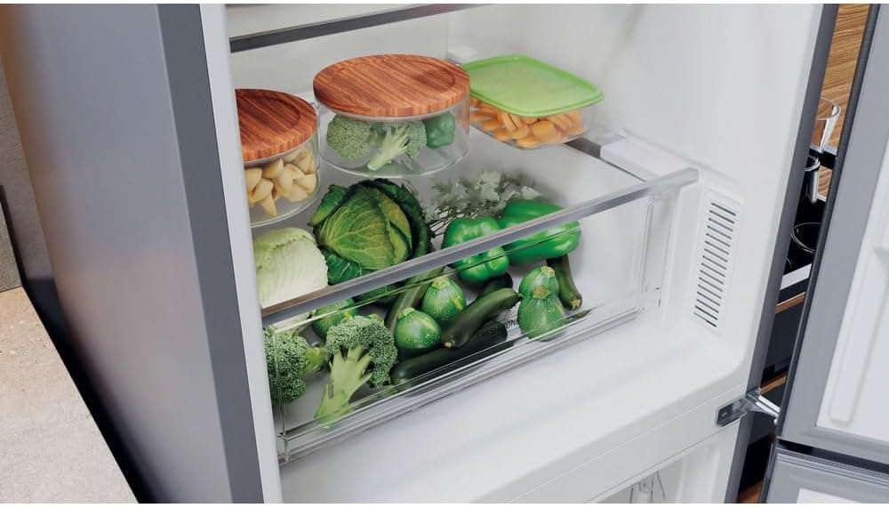 Close-up of the crisper drawer filled with fresh vegetables inside the Hotpoint refrigerator.