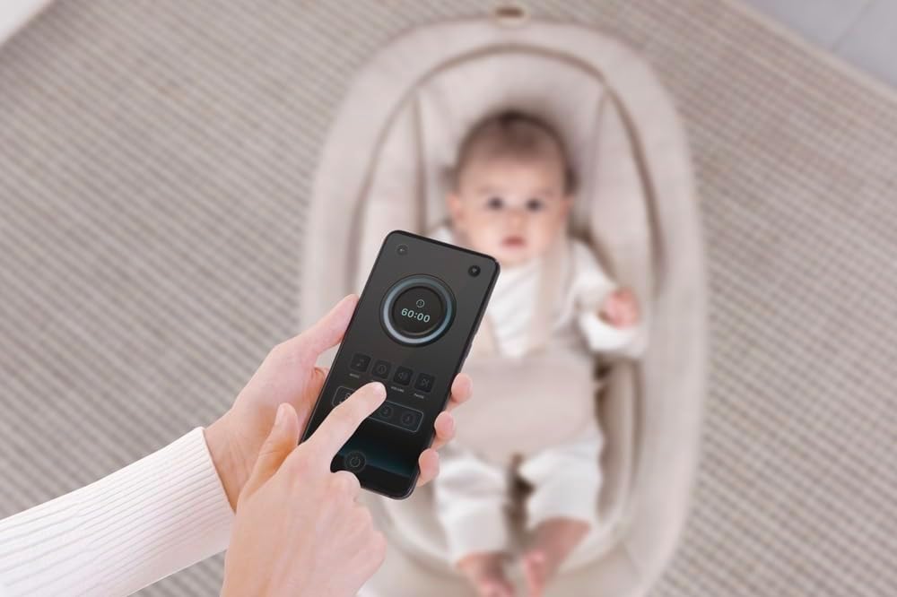 A hand holding the remote control for the Mastela Lullaby Orbit rocker, with a baby in the background.