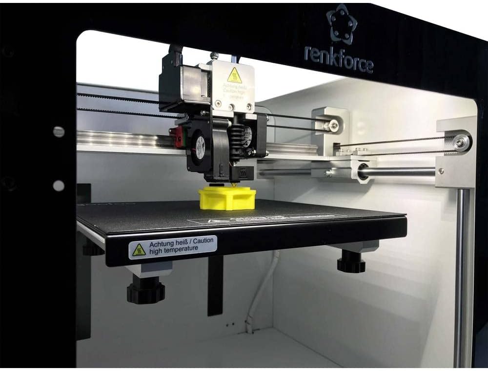 Close-up of the Renkforce PRO3 3D Printer's print head and build plate, actively printing a small yellow object.