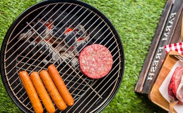 Hot dogs and a hamburger patty cooking on the grill grate of the portable charcoal grill