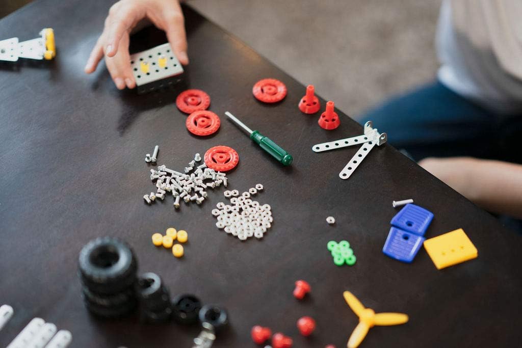Various metal and plastic parts of the erector set, including screws, nuts, plates, and tools, neatly arranged on a table.
