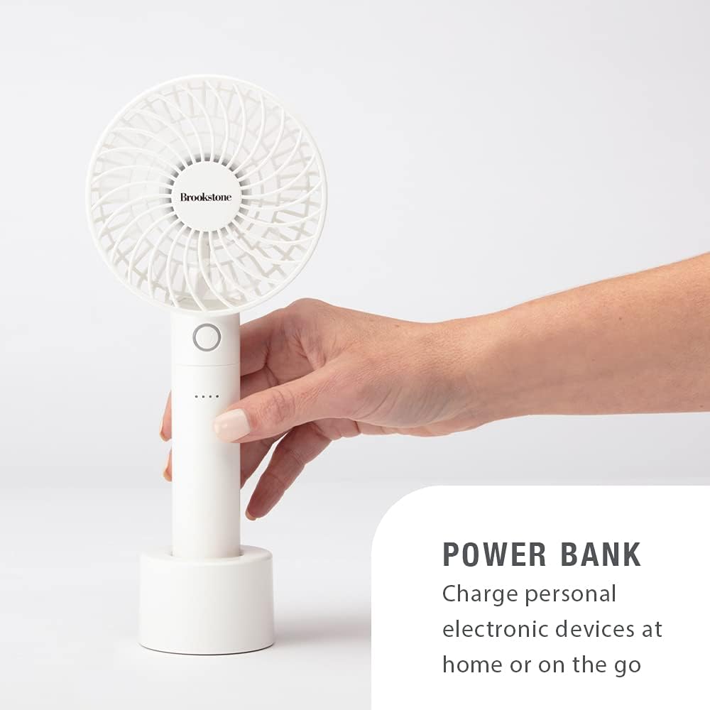 A hand holding the Brookstone fan, demonstrating its use as a power bank. The fan is shown connected to a charging cable, ready to charge another device.