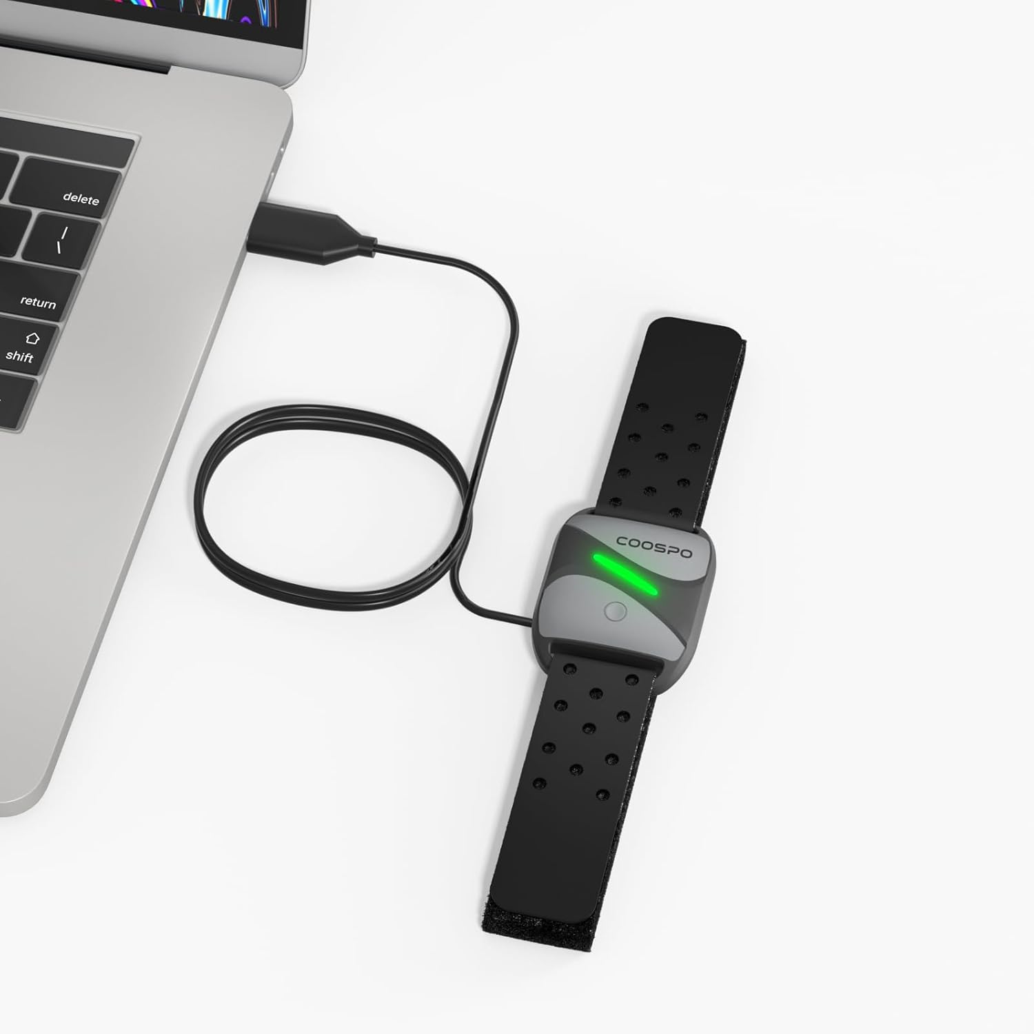 CooSpo heart rate monitor armband charging via USB cable connected to a laptop.