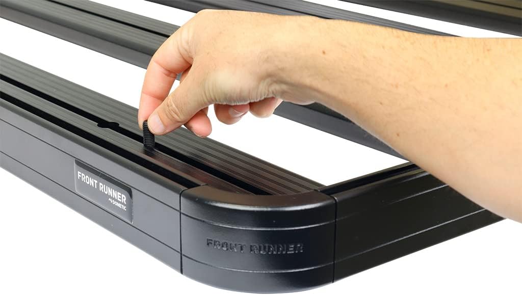 A hand inserting a bolt into the T-slot of the Front Runner Slimline II roof rack, demonstrating the securing mechanism.