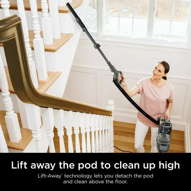 A woman using the Shark Lift-Away vacuum in portable mode to clean high areas, holding the wand with an attachment.