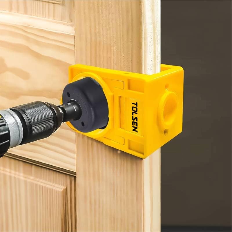 A person drilling the latch bolt hole on the edge of a wooden door using a cordless drill and the TOLSEN positioning frame as a guide.