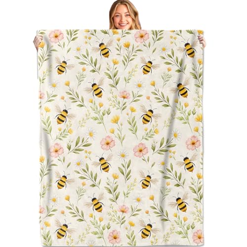 A folded flannel throw blanket printed with bees and wildflowers on a couch