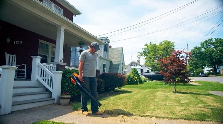 Man using leaf blower to clear leaves from a sidewalk