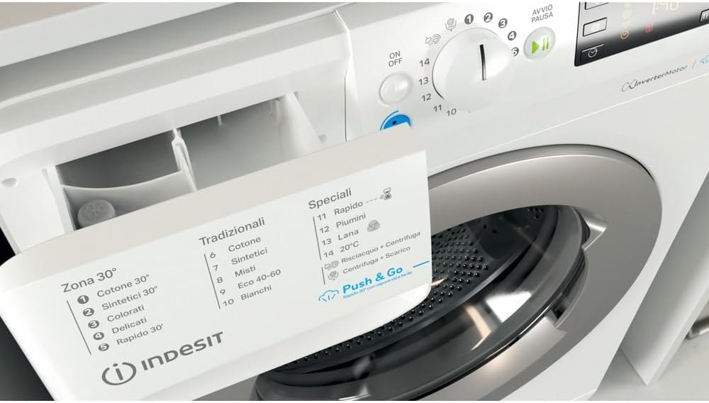 Avvicinamento view of the open detergent dispenser drawer of the Indesit washing machine, revealing compartments for detergent and softener, with a program list visible on the machine's top panel.