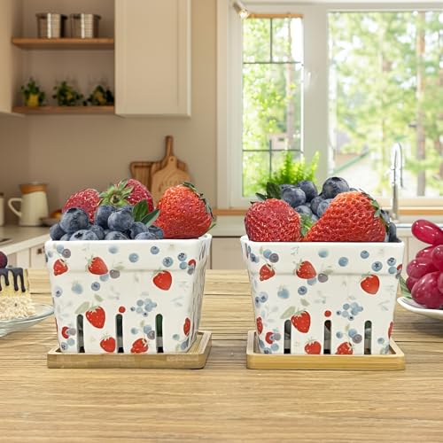 Two berry-patterned ceramic baskets filled with strawberries, blueberries, and raspberries on a kitchen counter