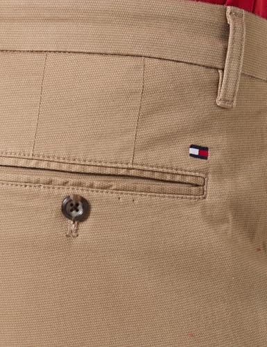 Primer plano del botón y la bandera de Tommy Hilfiger en la parte trasera del pantalón chino beige, destacando la calidad del acabado.