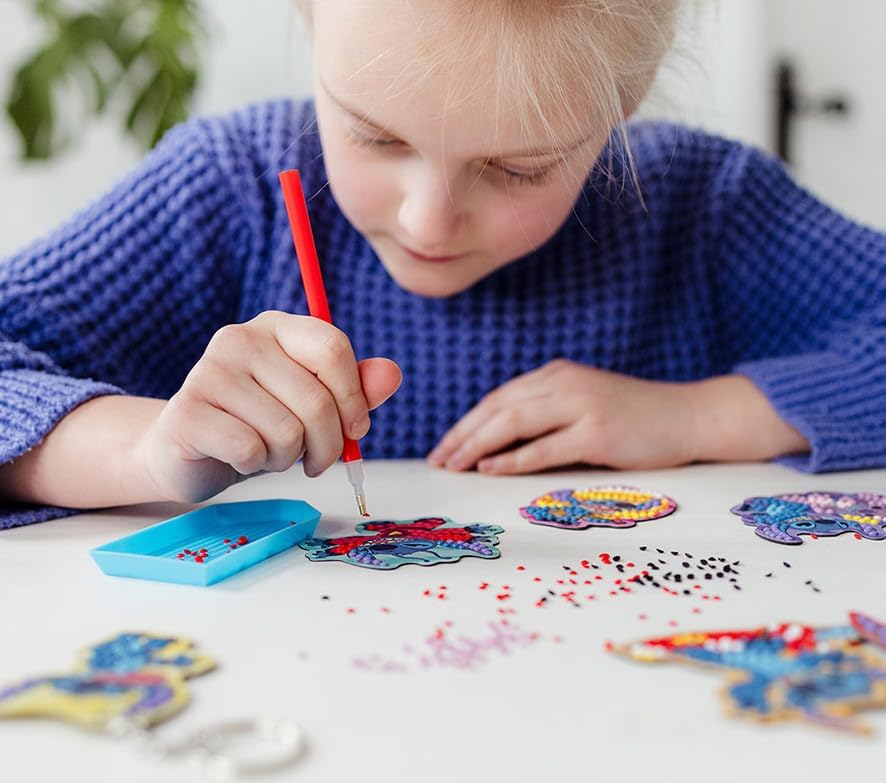 Child applying diamond gems to a Stitch magnet base with an applicator pen