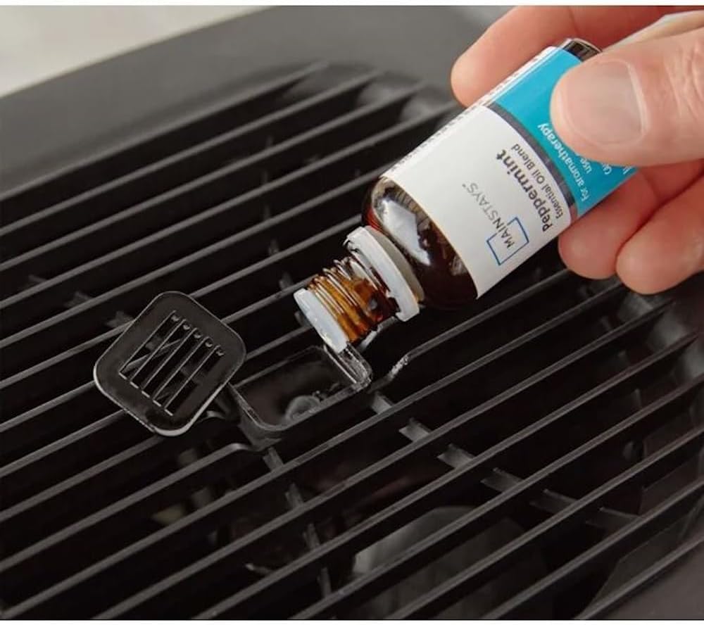 A hand pouring essential oil from a bottle into the aroma tray of the humidifier.