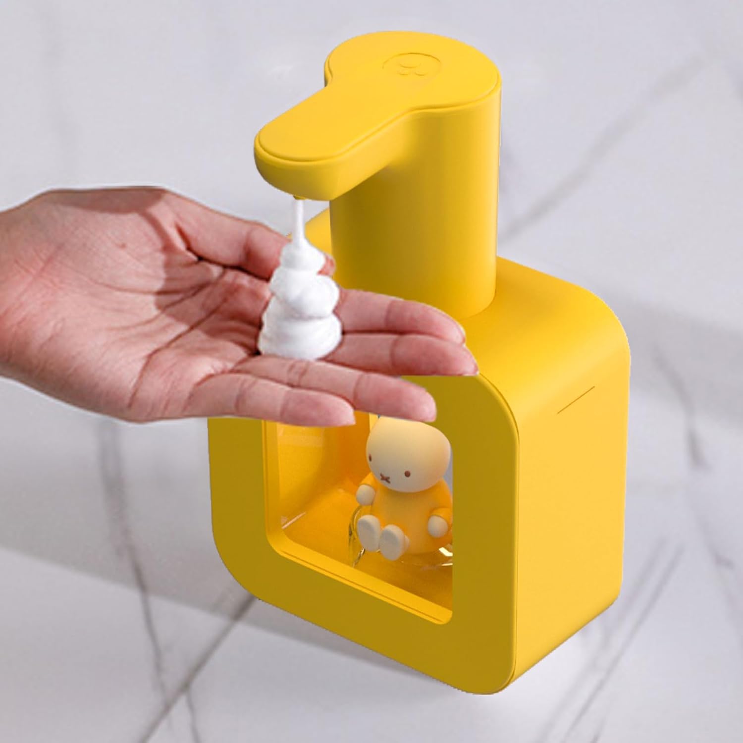 A hand placed under the nozzle of the Miffy Automatic Hand Soap Dispenser, receiving a dollop of foam.