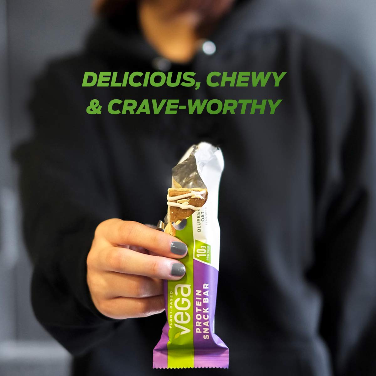 A person holding an unwrapped Vega Protein Snack Bar, highlighting its chewy texture.