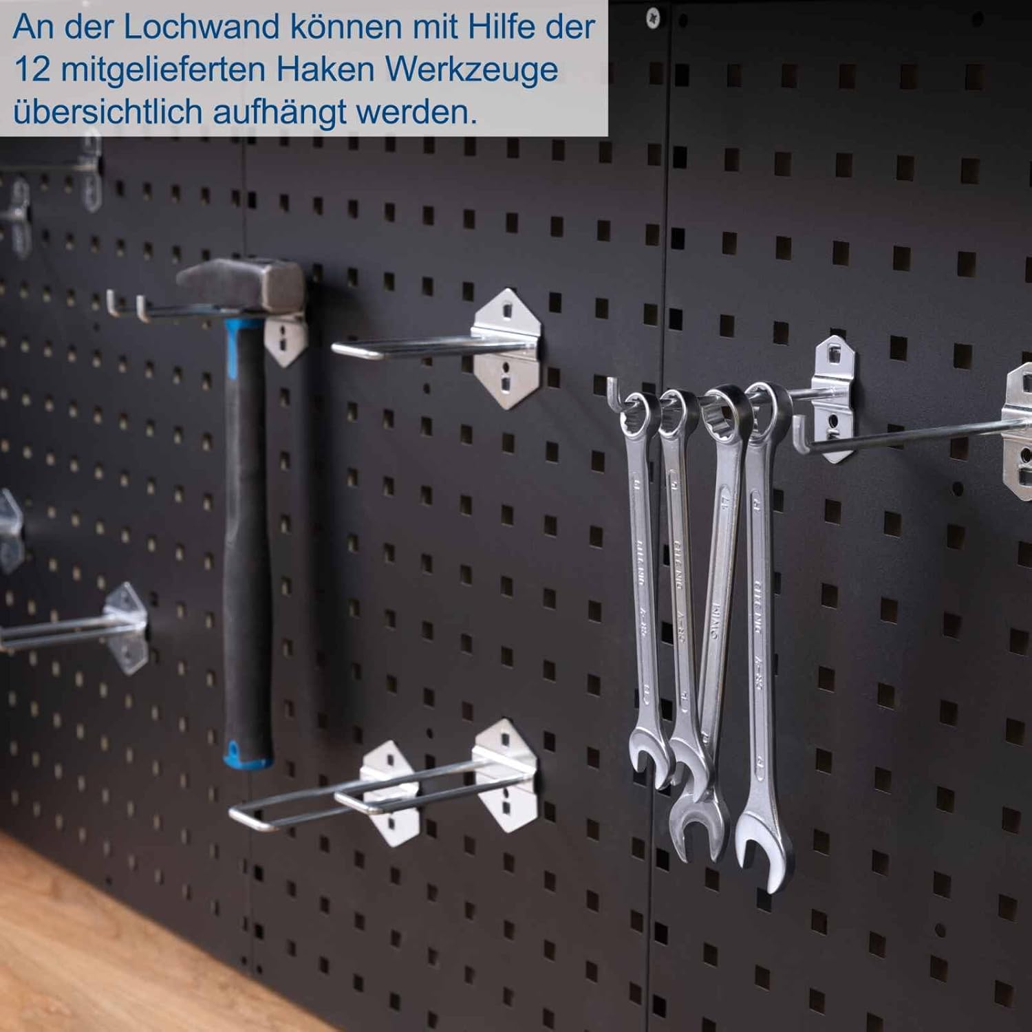Various tools, including wrenches and a hammer, hanging neatly on the black perforated panel with hooks.