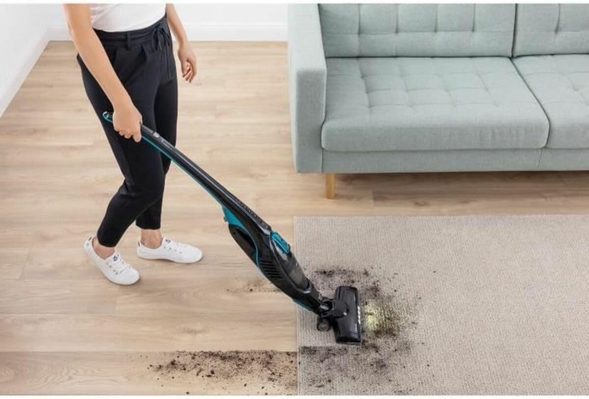 Person using SENCOR SVC 7822TQ stick vacuum on a carpet, showing LED lights illuminating the floor